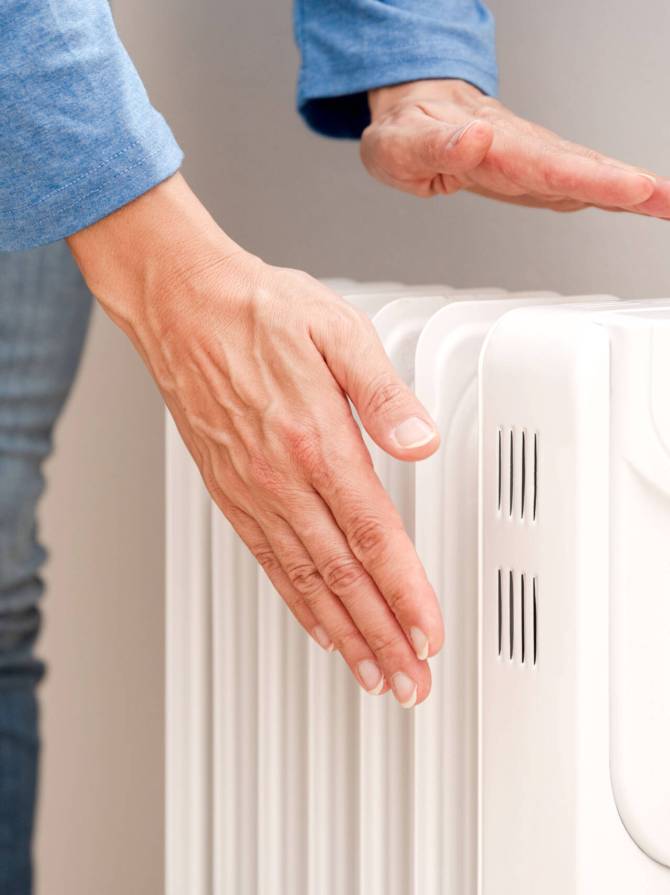 close up of Person Warming Hands Over a White Electric Radiator, Home Heating and Energy Efficiency concept close up of Person Warming Hands Over a White Electric Radiator, Home Heating and Energy Efficiency concept